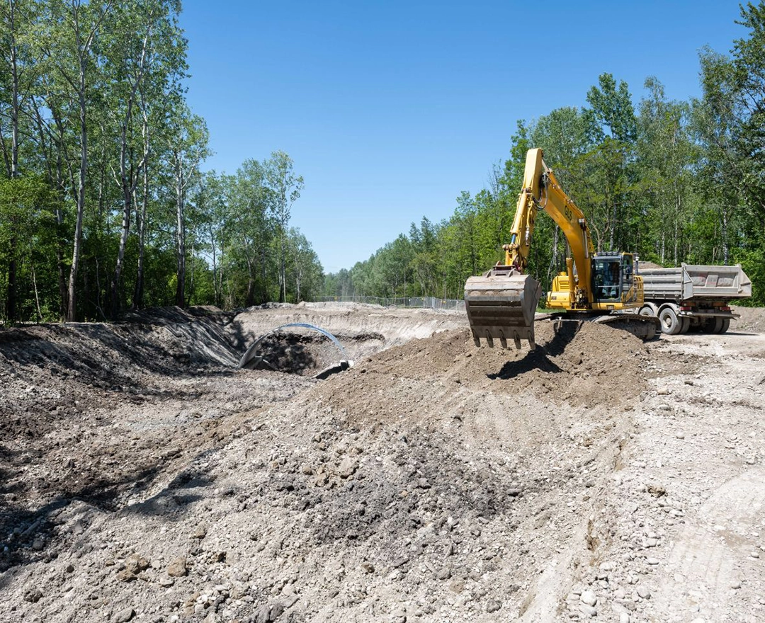 The first preparatory work for the Abwinden-Asten fish pass is being carried out: an excavator is fighting its way through the subsoil under a bright blue sky.